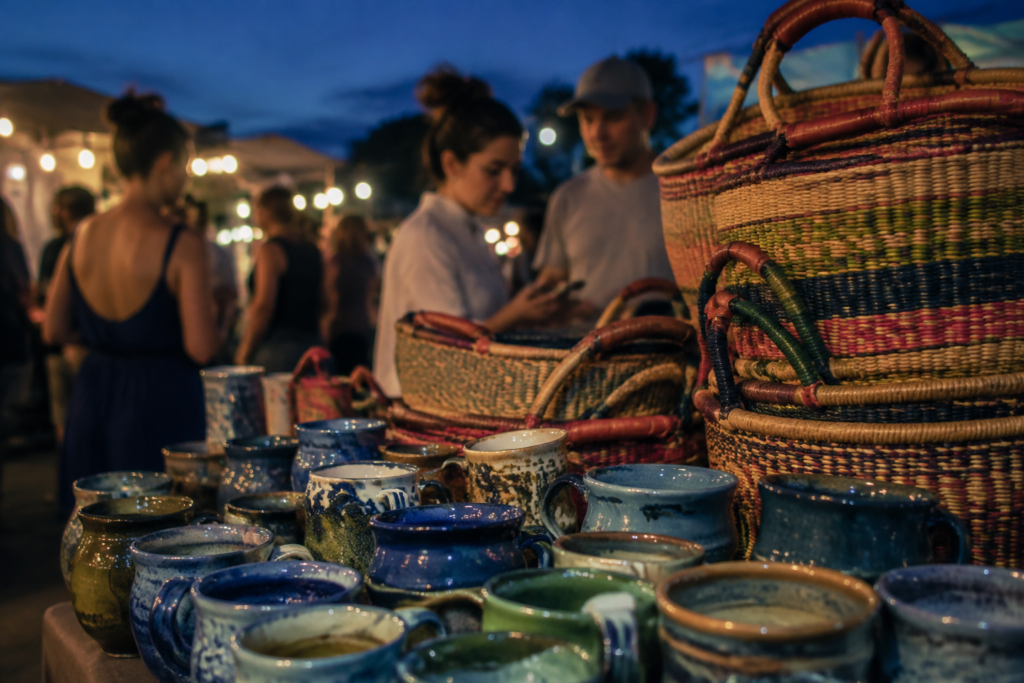 Handmade ceramic cups and colorful woven baskets at an outdoor artisan stall at blue hour