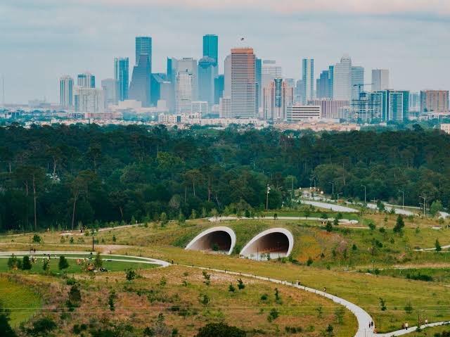 Green parkland and twin arched tunnels with the Houston skyline beyond