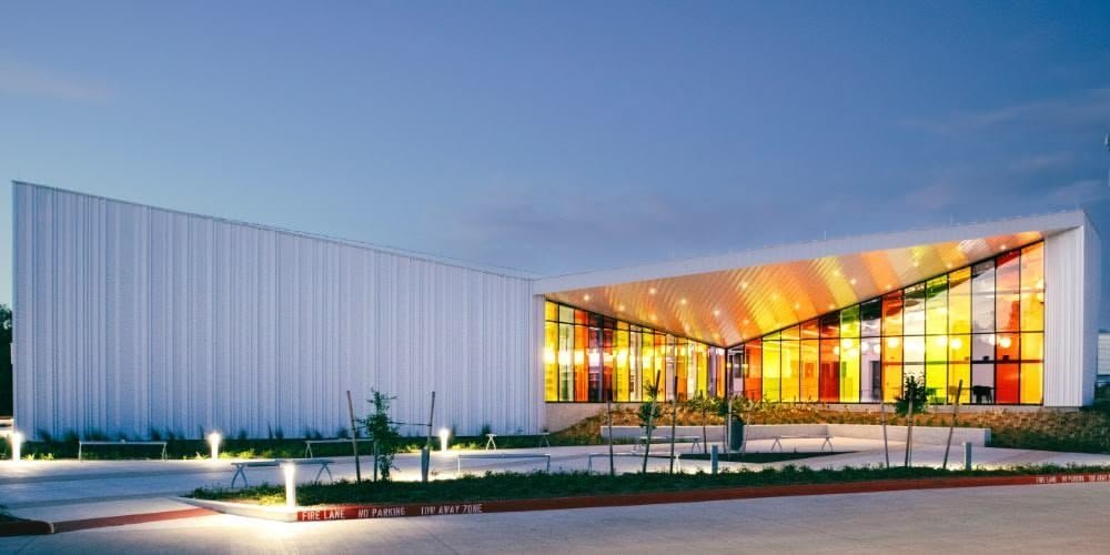 Modern building with colorful illuminated windows and landscaped entrance at dusk