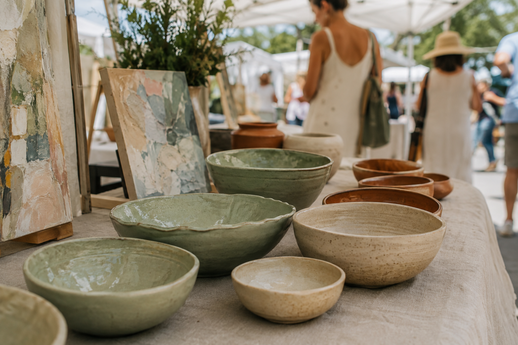 AI-generated illustration of handmade pottery and abstract paintings at an outdoor artisan stall.