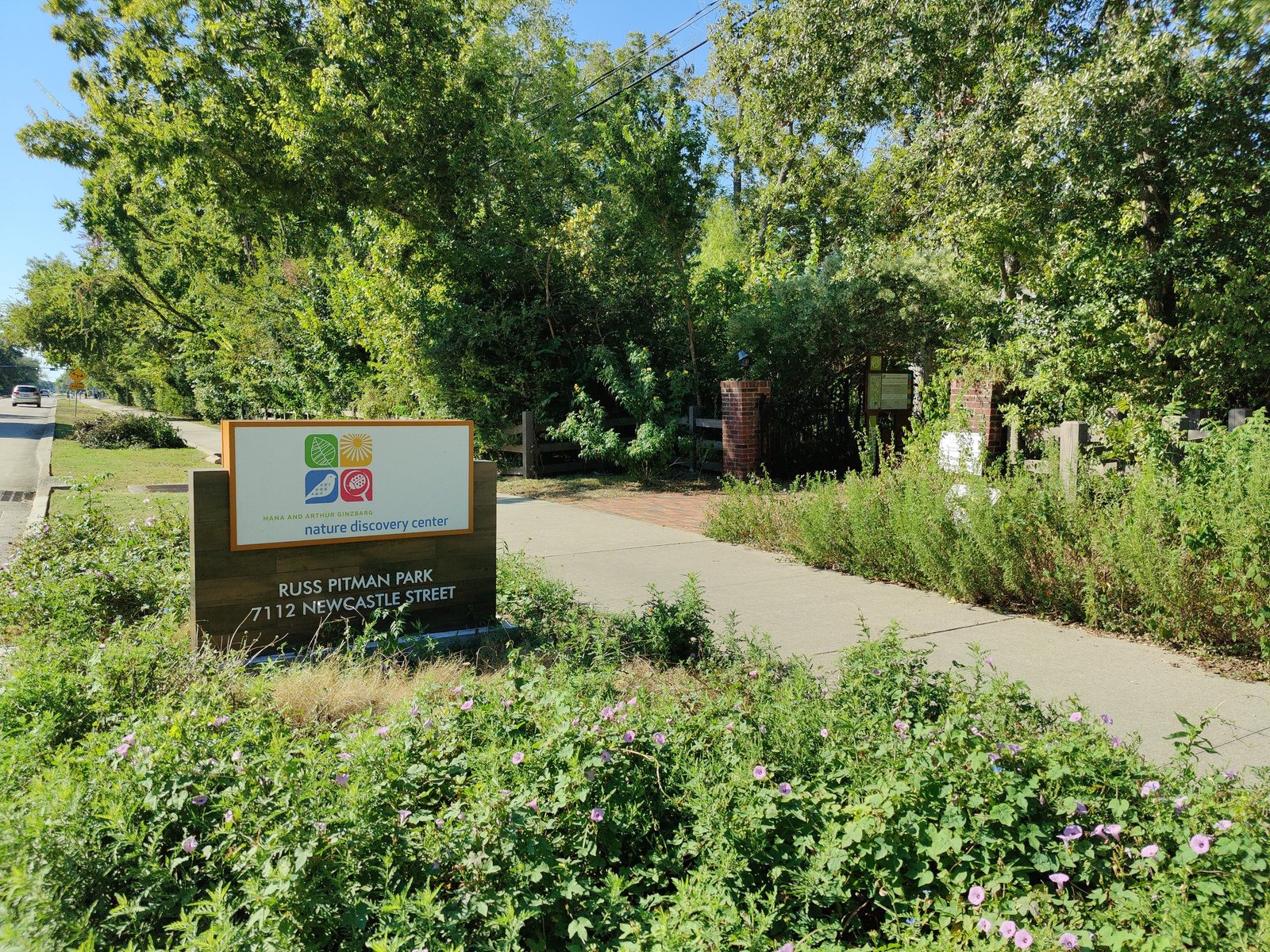The Nature Discovery Center sign at the Russ Pitman Park entrance on Newcastle Street in Bellaire, with a shaded walk leading to the gate.