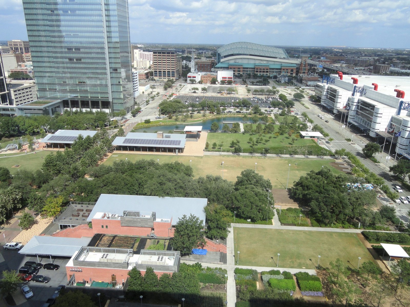 Aerial view of Discovery Green park in downtown Houston, with its lawns, pond and the George R. Brown Convention Center beside it.