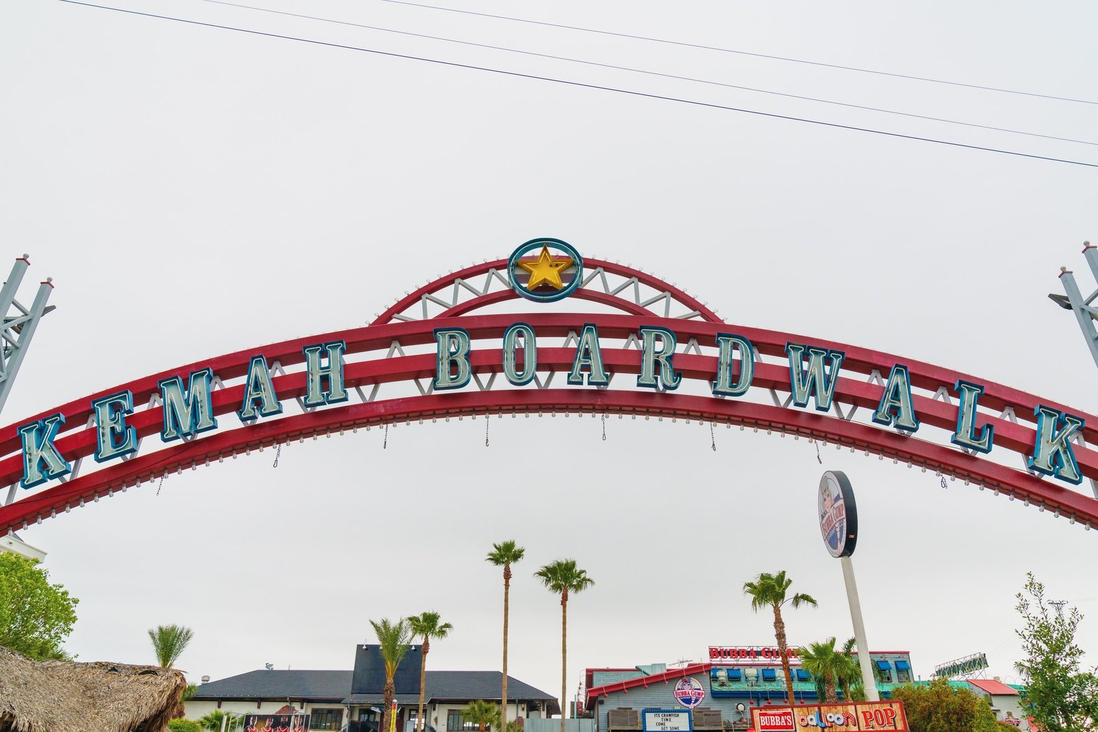 The red Kemah Boardwalk entrance arch with palm trees under an overcast sky in Kemah, Texas.