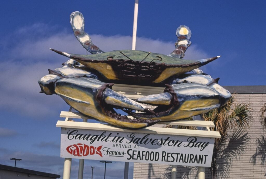 Gaido's crab sign on Seawall Boulevard in 1986, a giant painted blue crab above a sign reading Caught in Galveston Bay, served at Gaido's Famous Seafood Restaurant