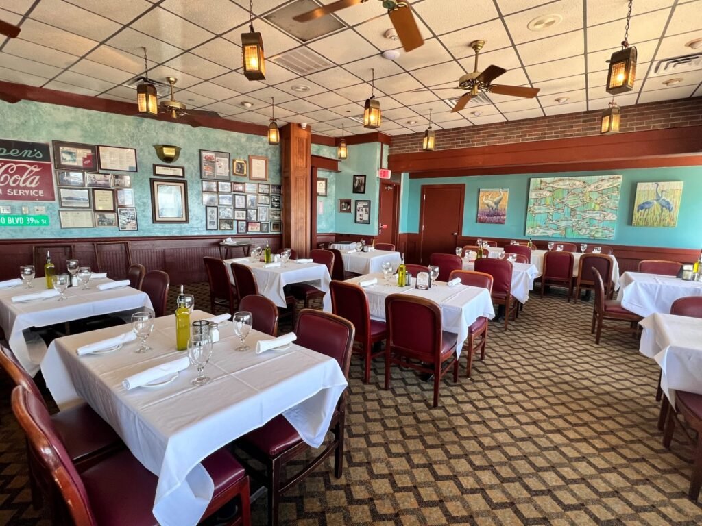 The dining room at Gaido's in Galveston, with white-clothed tables, burgundy chairs, hanging lanterns and a wall of framed photos from the restaurant's history