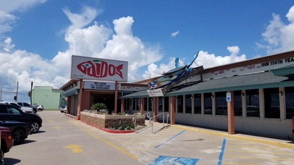 The front of Gaido's Famous Seafood Restaurant on Seawall Boulevard in Galveston, with its red Gaido's sign, the entrance and the giant blue crab on the roof