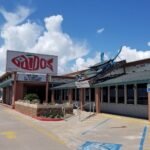 The front of Gaido's Famous Seafood Restaurant on Seawall Boulevard in Galveston, with its red Gaido's sign, the entrance and the giant blue crab on the roof