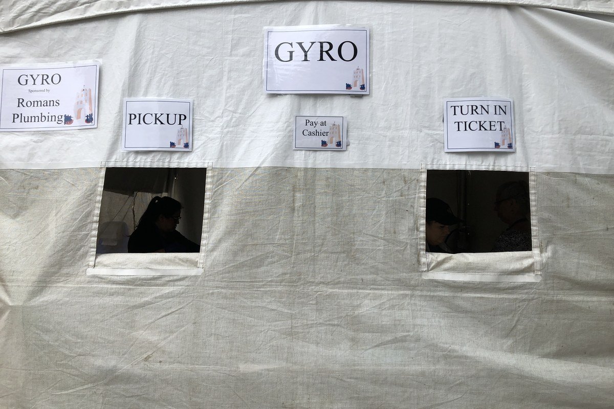 Outdoor Greek festival gyro / street-food tent with coals and pita service — licensed food-tent atmosphere; photographed at the 2019 Marin Greek Festival (Novato, CA), not the 2026 Galveston festival