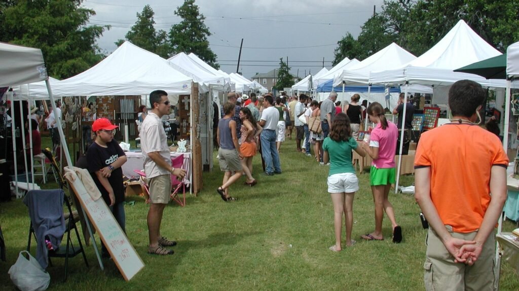 Visitors browsing art booths beneath white tents at an outdoor festival