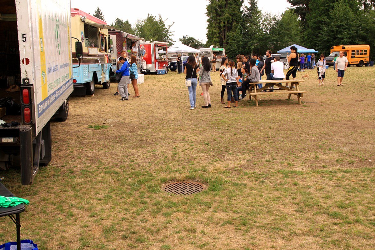 Line of food trucks and visitors on an open grassy festival field — licensed food-truck park atmosphere; not a documentary of the 2026 Bayou City Art Festival Memorial Park food vendors