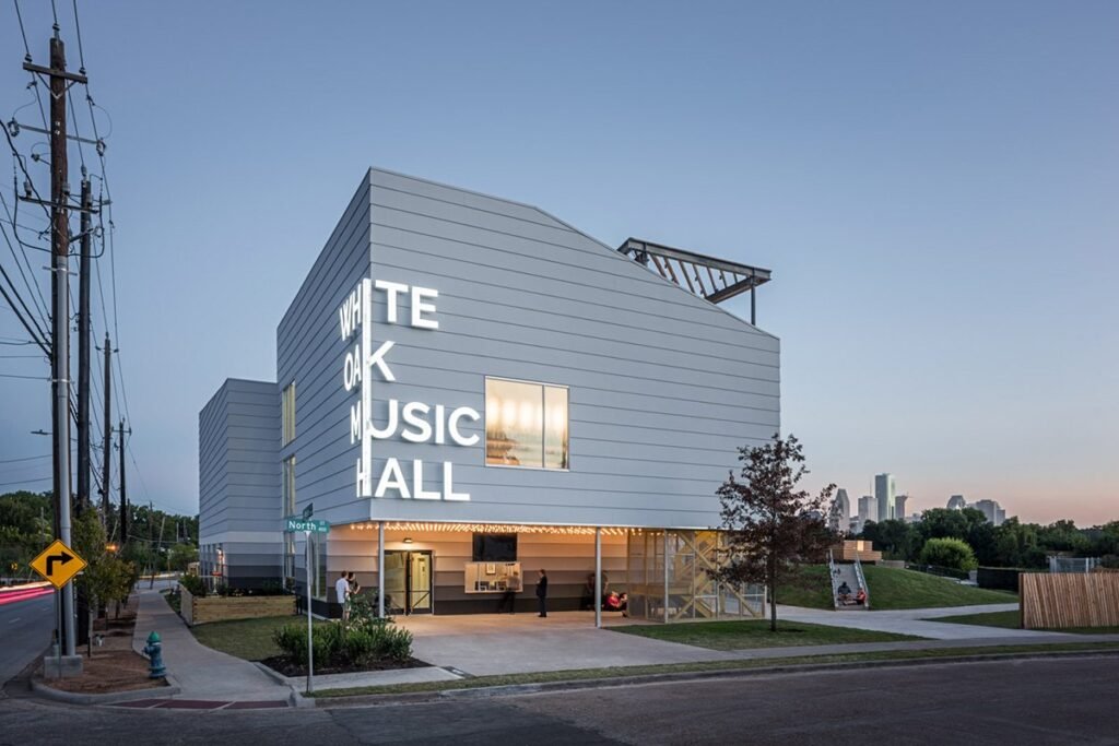 White Oak Music Hall's neon sign and entrance at dusk on N. Main St., with the downtown Houston skyline behind it