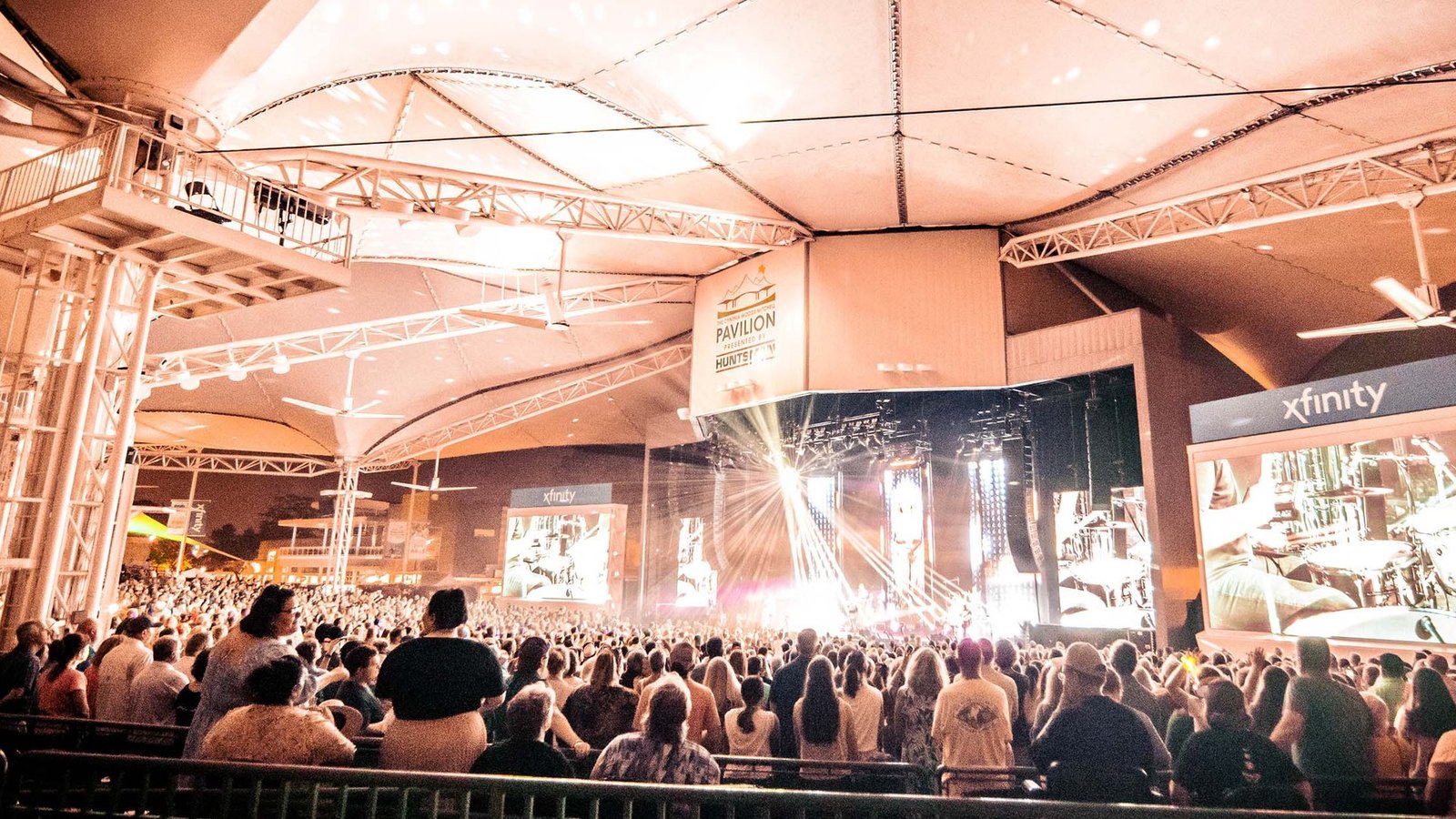 The Pavilion audience standing under the white canopy as a band plays on the lit main stage