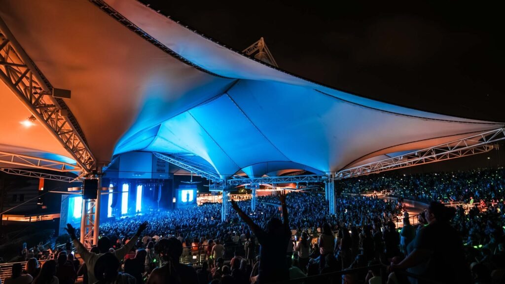 A packed crowd under the lit canopy of the Cynthia Woods Mitchell Pavilion during a night concert