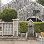 The front of the Beer Can House in Houston, its walls hung with flattened beer cans behind a can-covered fence and trimmed hedges
