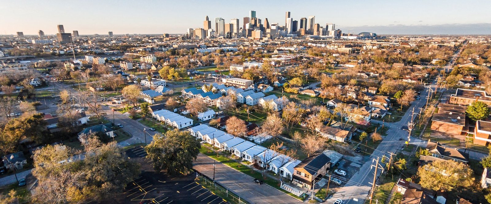 An aerial view of Project Row Houses, rows of small white houses in Houston's Third Ward with the downtown skyline behind