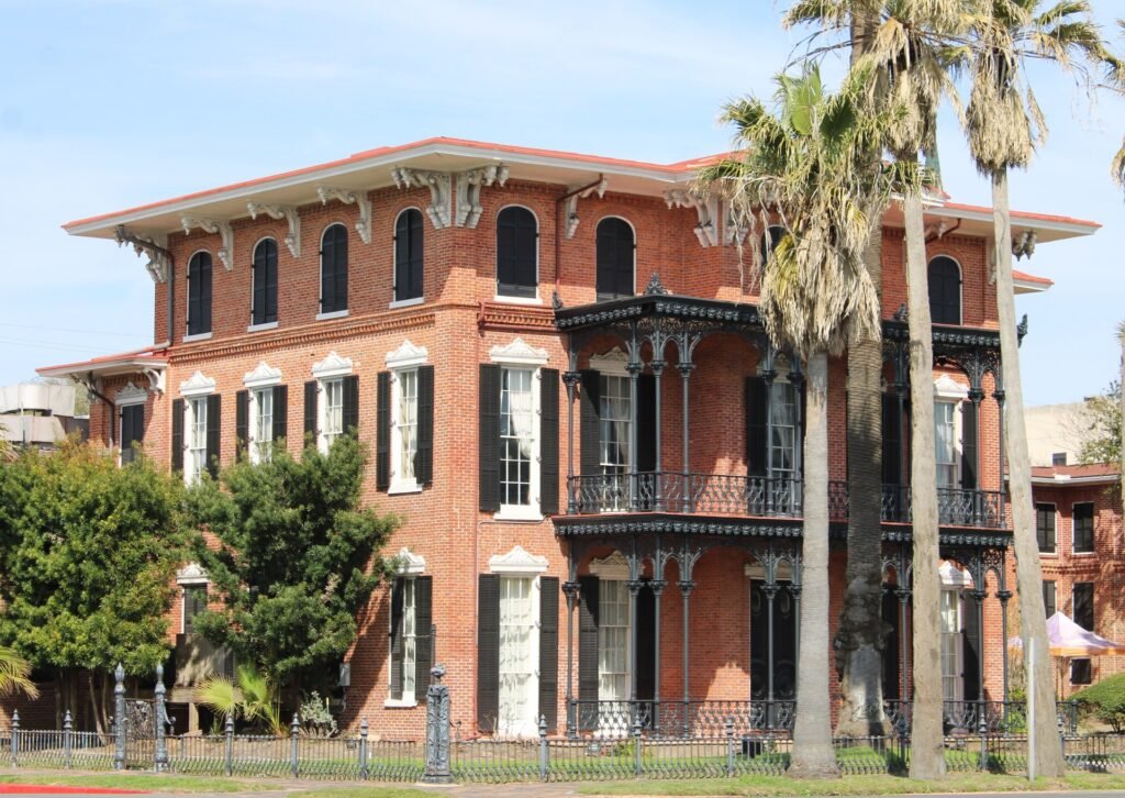 Ashton Villa, the 1859 red-brick Italianate mansion on Broadway in Galveston, with iron balconies and palm trees.