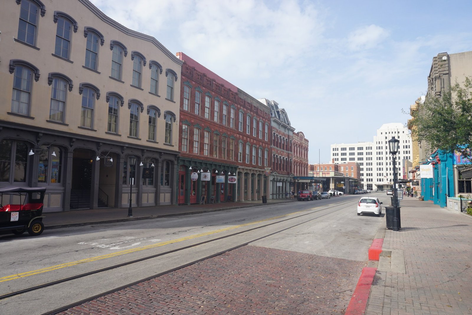 The Strand in downtown Galveston's Strand Historic District, with brick commercial buildings, iron-front storefronts and a brick-paved trolley lane.